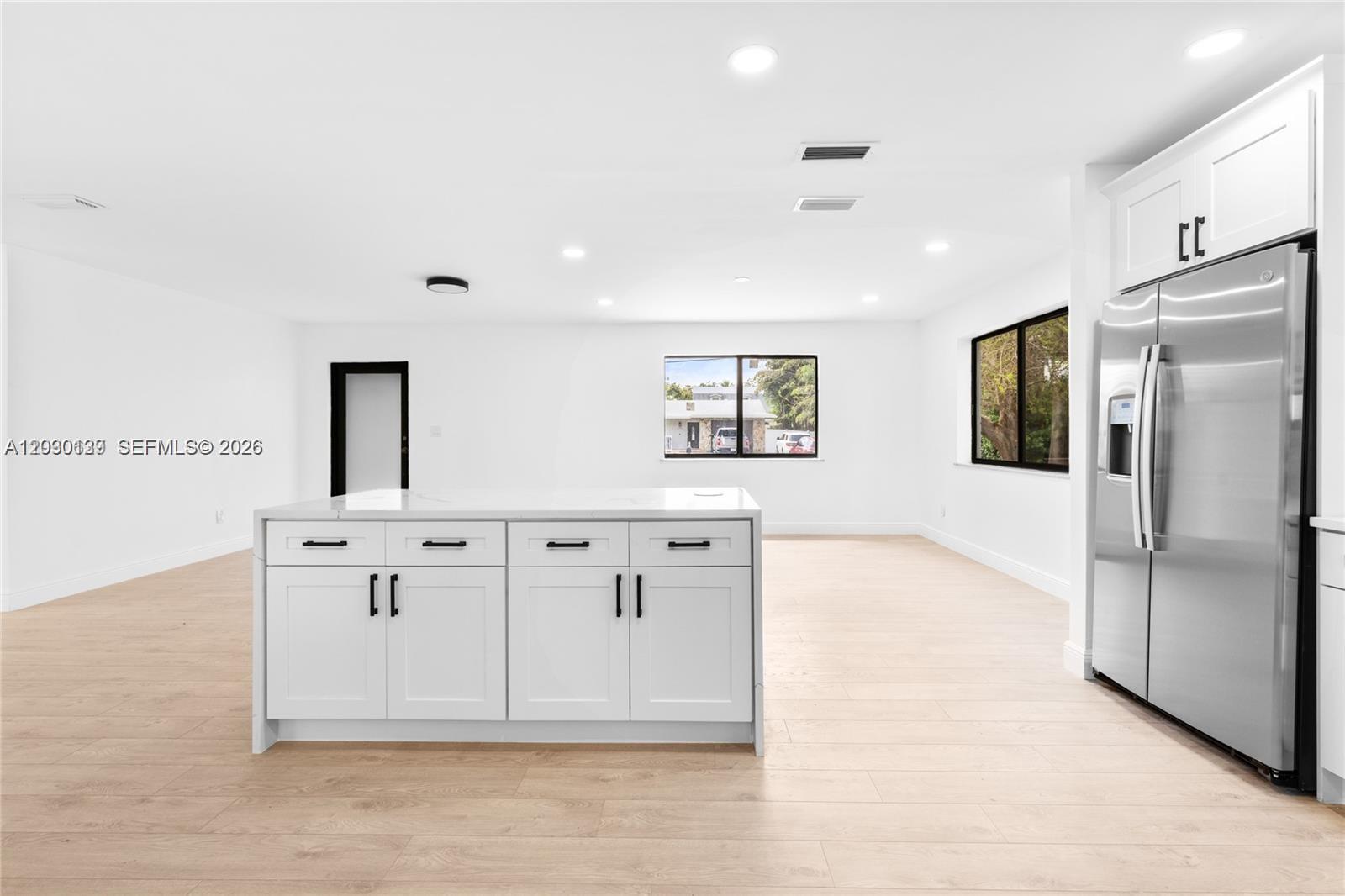 A modern kitchen features a white island, stainless steel refrigerator, and light wood flooring — 14171 SW 37th Ct, Davie FL 33330, DAVIE, FL