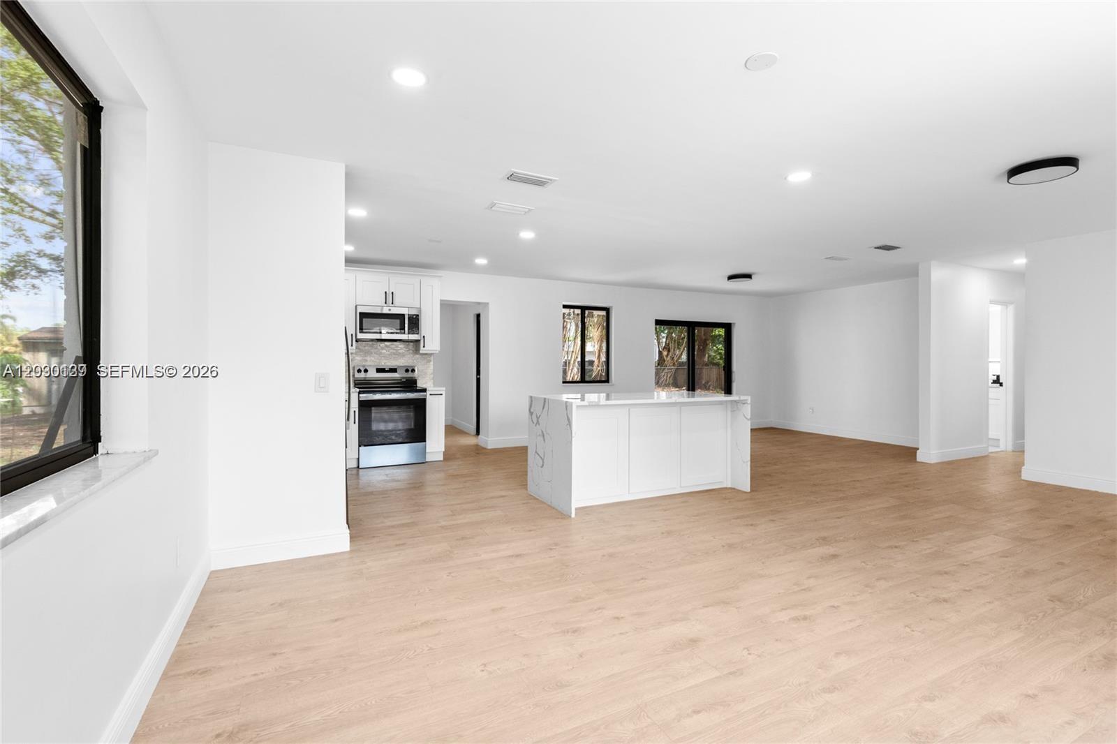 This open-concept kitchen and living area features white cabinetry, a marble-topped island, and light flooring — 14171 SW 37th Ct, Davie FL 33330, DAVIE, FL