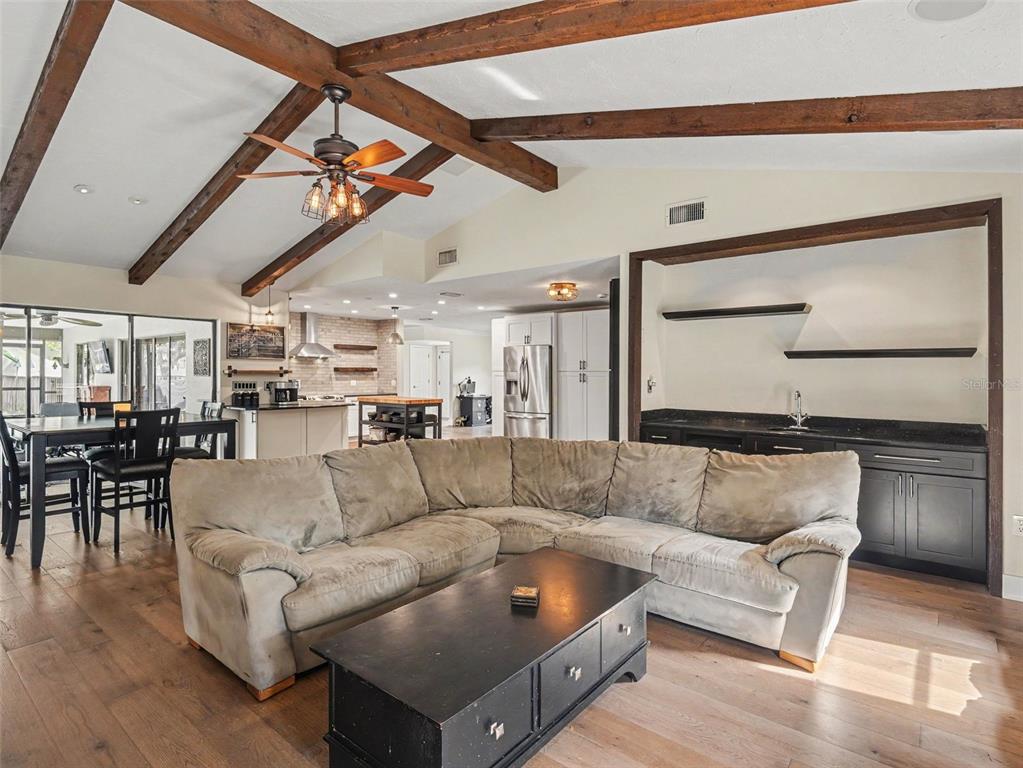 A living room features a sectional sofa, wooden ceiling beams, and an adjacent kitchen area — 3911 COUNTRY VIEW CIR, SARASOTA, FL