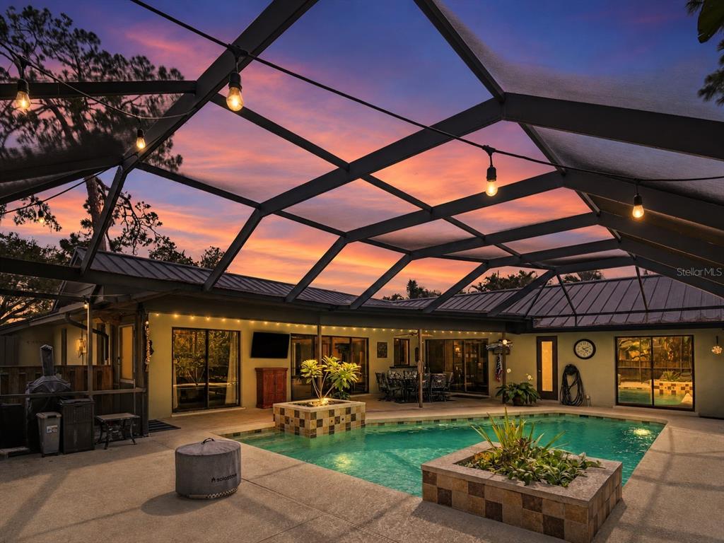 A screened-in patio features a swimming pool with two tiled planters under a sunset sky — 3911 COUNTRY VIEW CIR, SARASOTA, FL