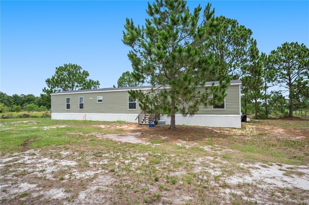 A light green manufactured home sits on a sandy, grassy lot with pine trees — 4770 SUGARFOOT AVENUE, LAKE WALES, FL