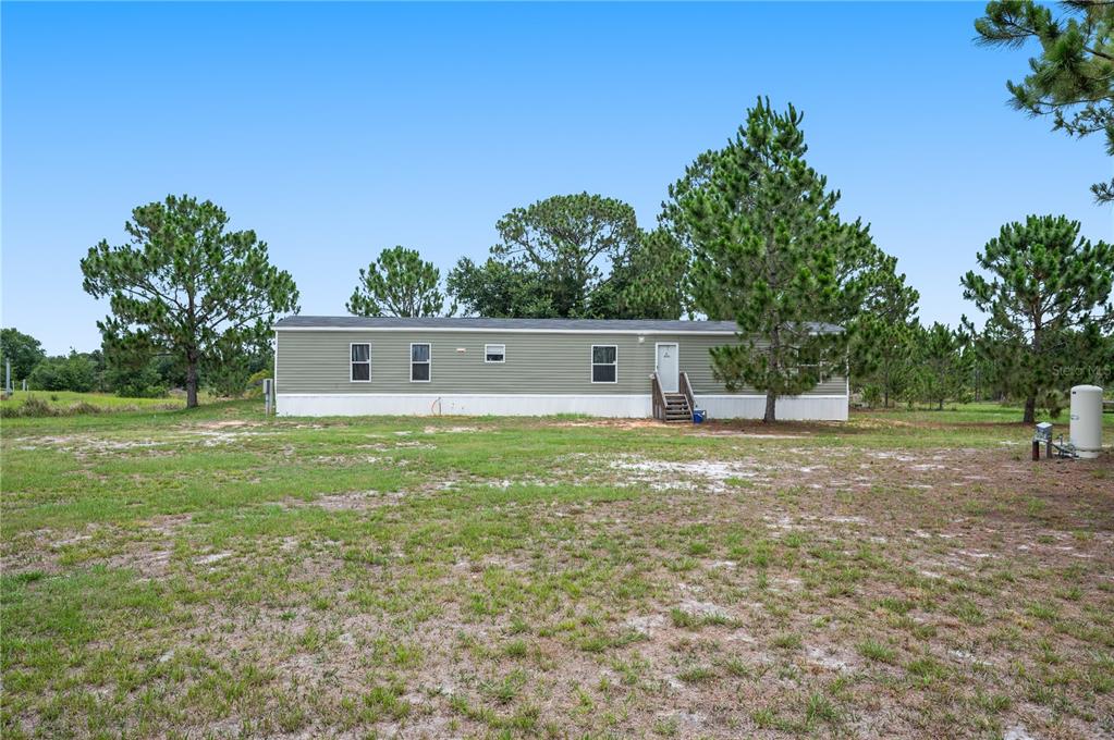 A long, green manufactured home sits on a large, grassy lot with scattered pine trees — 4770 SUGARFOOT AVENUE, LAKE WALES, FL
