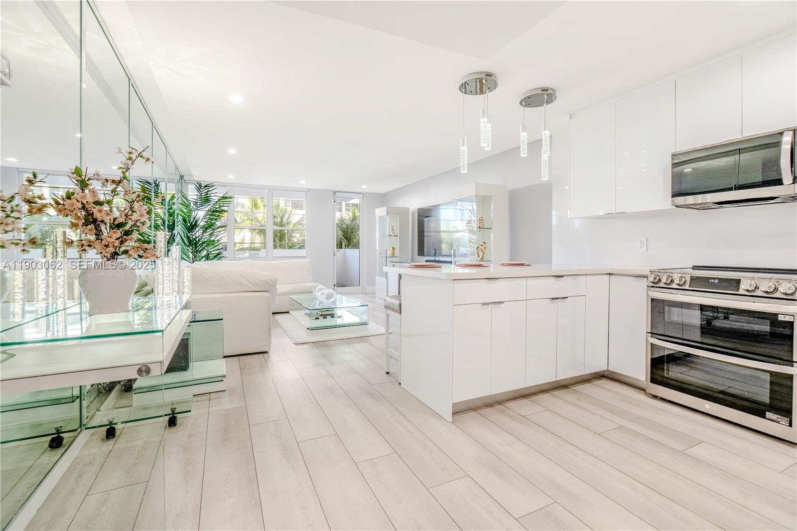 A modern, open-concept kitchen and living area features white cabinetry, stainless steel appliances, and flooring — 100 Lincoln Rd # 323, Miami Beach FL 33139, MIAMI BEACH, FL