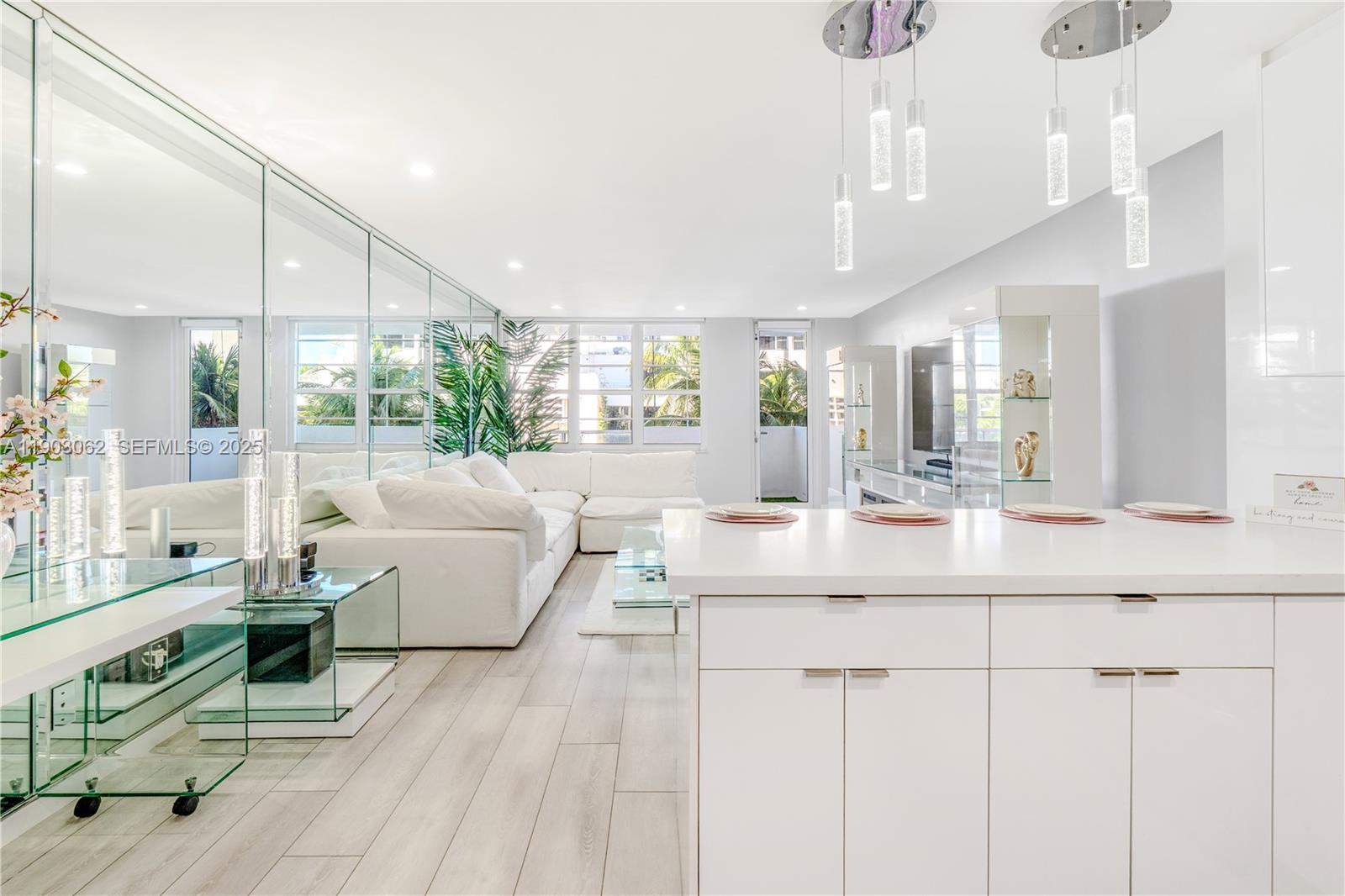 A modern, white-themed living room and kitchen area features mirrored walls and light wood flooring — 100 Lincoln Rd # 323, Miami Beach FL 33139, MIAMI BEACH, FL