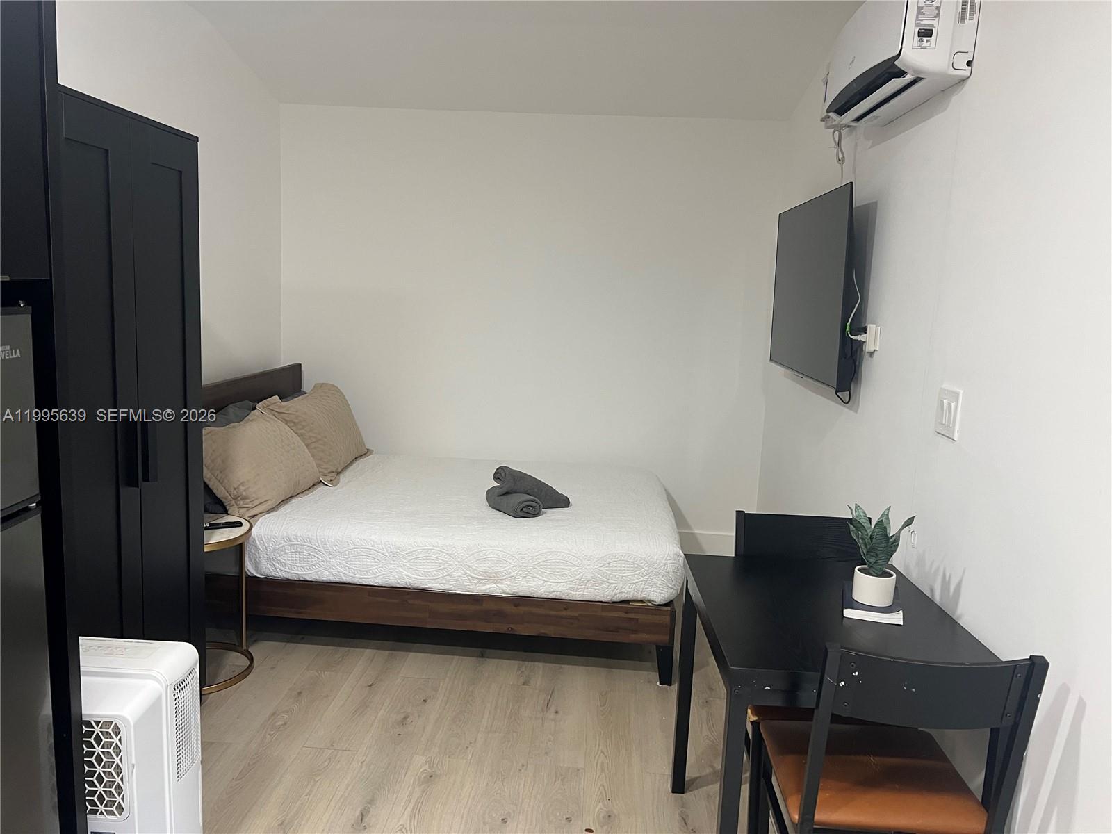 A small bedroom features a bed, a black wardrobe, a wall-mounted television, and a table — 2723 SW 13th St, Miami FL 33145, MIAMI, FL