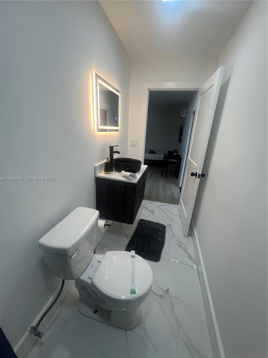 A small bathroom features a white toilet, a dark vanity with a vessel sink, and marble-look flooring — 2723 SW 13th St, Miami FL 33145, MIAMI, FL