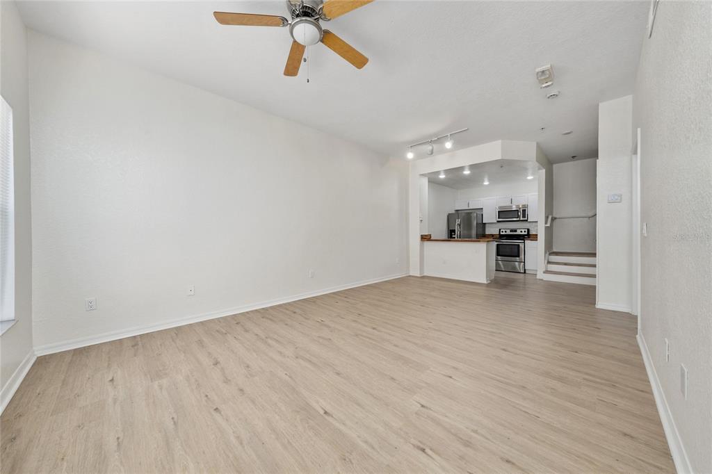 An open-concept living room with light wood-look flooring leads to a kitchen with stainless appliances — 2611 GALA ROAD N UNIT 106, KISSIMMEE, FL