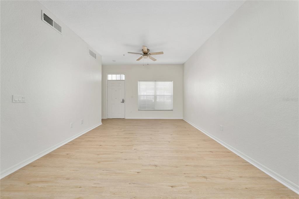 An empty living room features light wood-look flooring, white walls, and a ceiling fan — 2611 GALA ROAD N UNIT 106, KISSIMMEE, FL