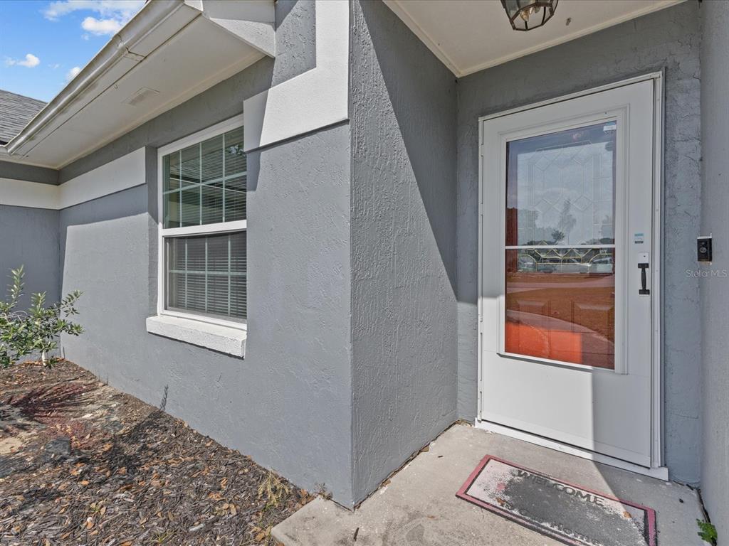A gray stucco exterior wall features a white-framed window and a white storm door — 226 WINDWARD WAY, DAVENPORT, FL