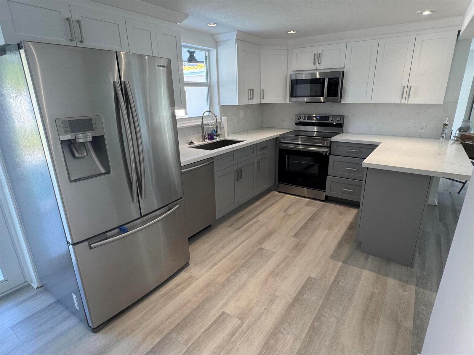 A kitchen features white upper cabinets, gray lower cabinets, stainless steel appliances, and light flooring — 28 SW 9th Avenue, Boca Raton FL 33486, BOCA RATON, FL