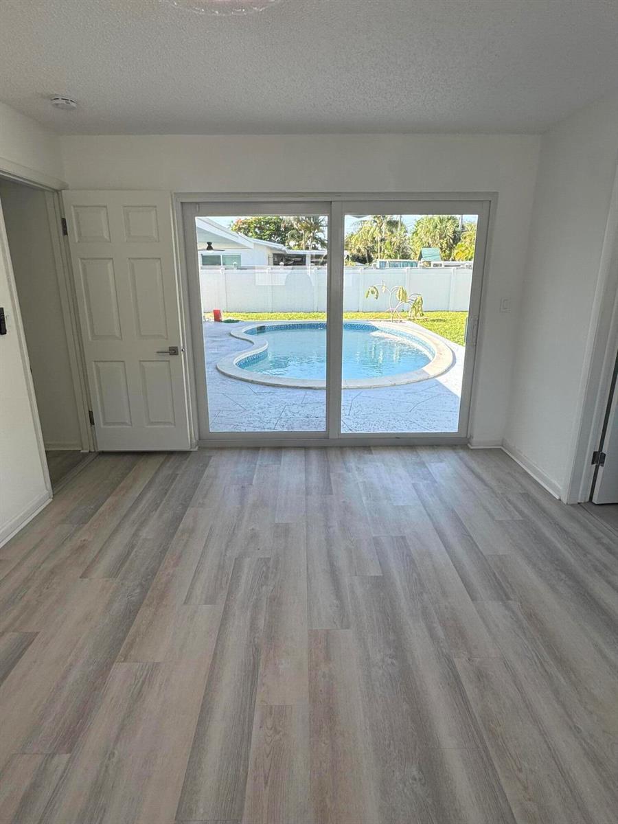 A room with light wood-look flooring and sliding glass doors overlooking a backyard swimming pool — 28 SW 9th Avenue, Boca Raton FL 33486, BOCA RATON, FL