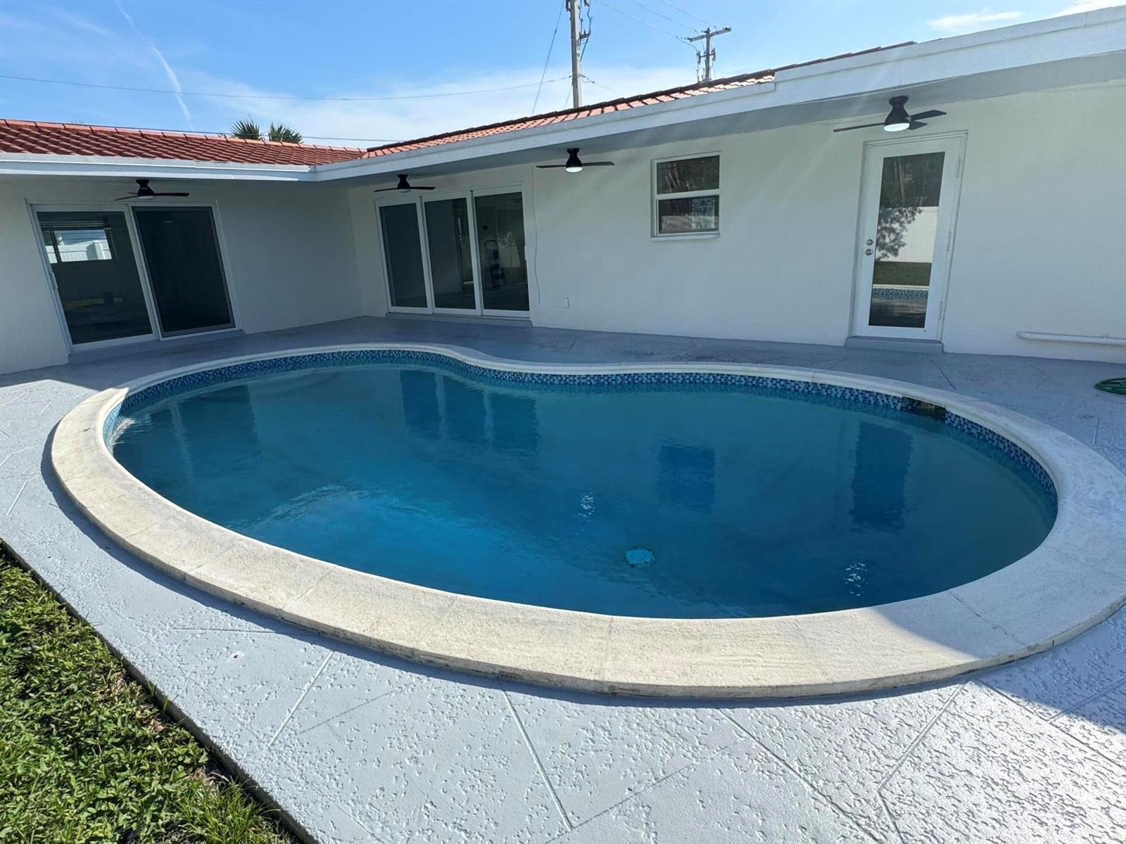 A kidney-shaped swimming pool sits on a concrete patio next to a white house — 28 SW 9th Avenue, Boca Raton FL 33486, BOCA RATON, FL