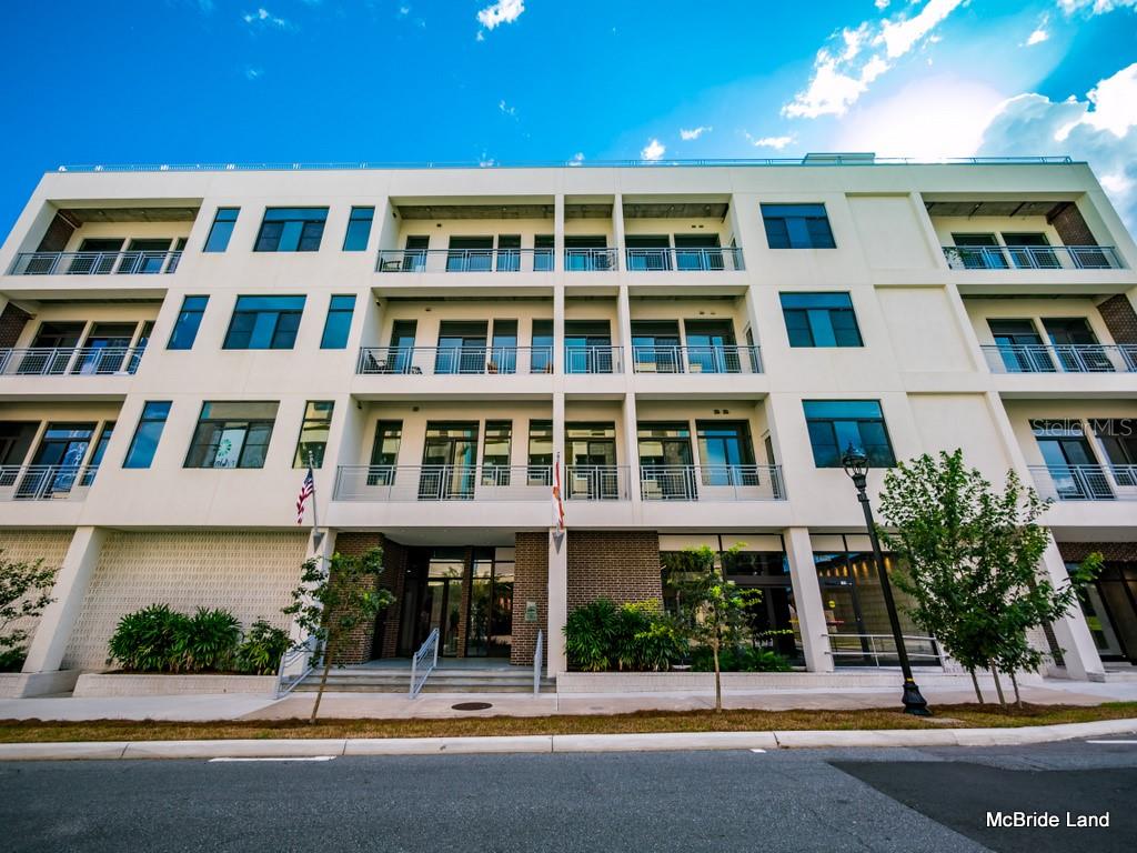 A low-angle exterior view of a modern four-story apartment building with balconies and brick accents — 302 SE BROADWAY STREET UNIT 110, OCALA, FL