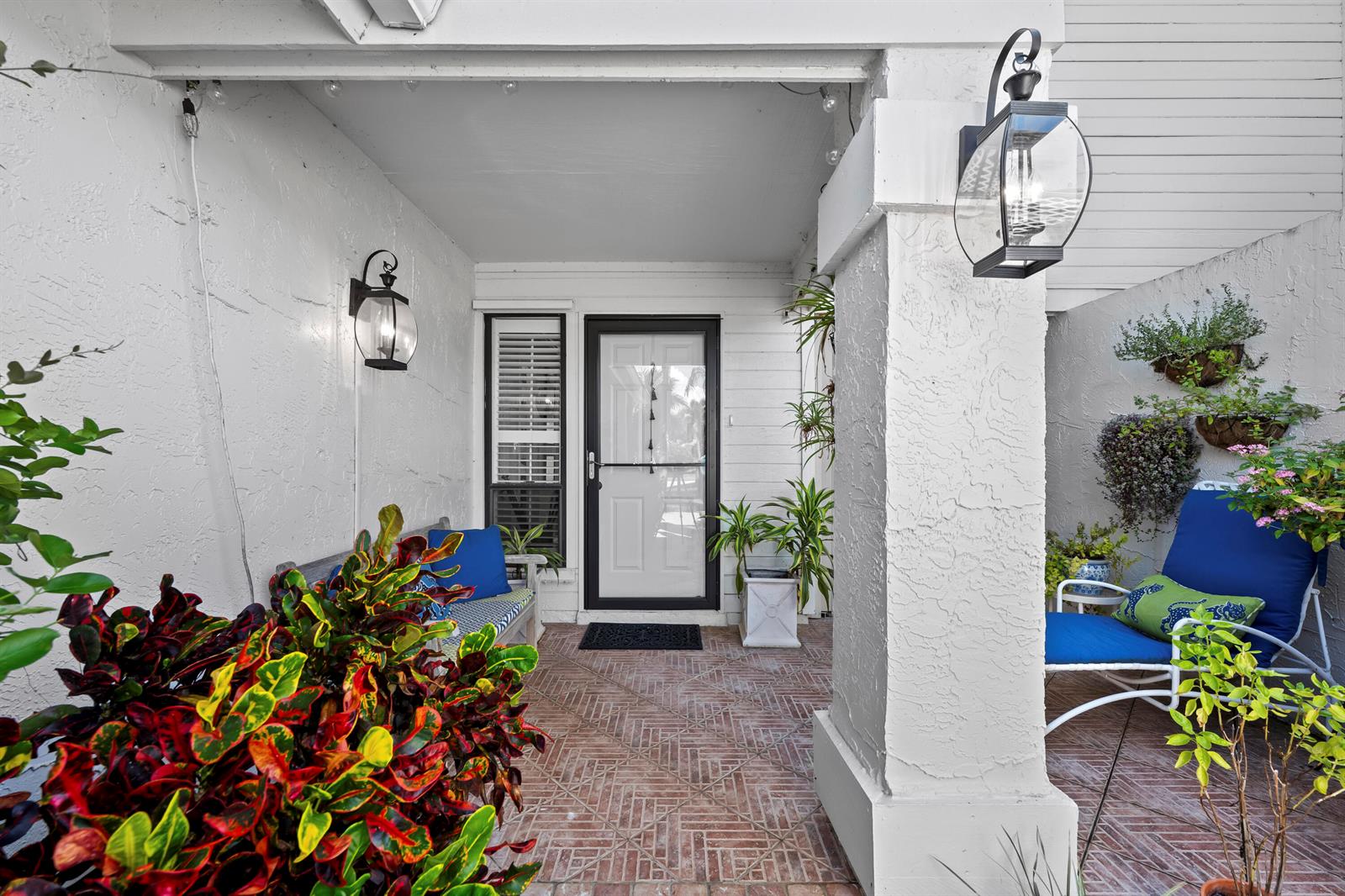 A covered front porch features brick flooring, white stucco walls, and two outdoor seating areas — 5610 SE Foxcross Place, Stuart FL 34997, STUART, FL