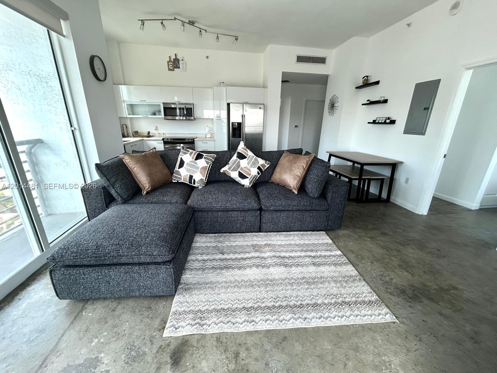 A living room features a dark gray sectional sofa, a patterned rug, and an open kitchen — 133 NE 2nd Ave # 3202, Miami FL 33132, MIAMI, FL