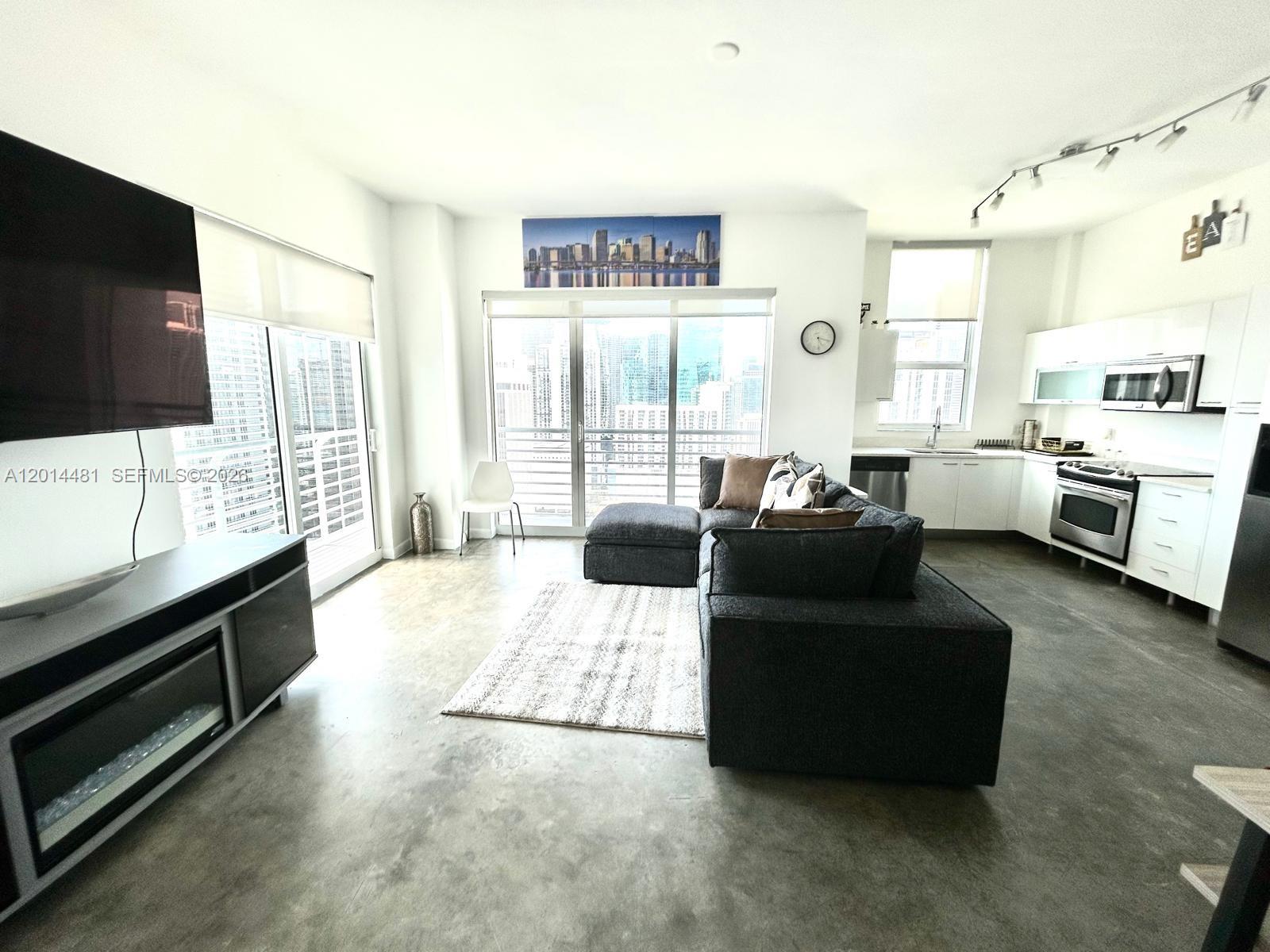 A modern open-concept living room and kitchen featuring concrete floors and floor-to-ceiling windows — 133 NE 2nd Ave # 3202, Miami FL 33132, MIAMI, FL