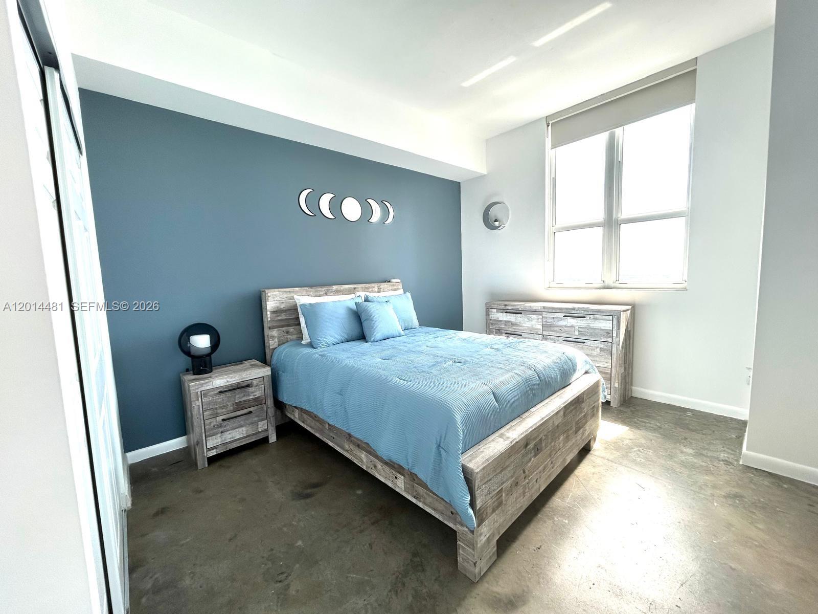 A bedroom features a blue accent wall, a wooden bed frame, and concrete flooring — 133 NE 2nd Ave # 3202, Miami FL 33132, MIAMI, FL