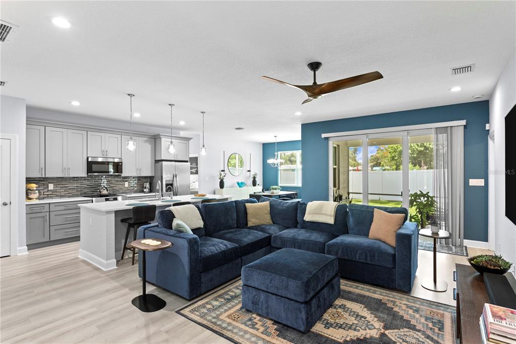 An open-concept living room and kitchen featuring a blue sectional sofa and gray cabinetry — 5220 94TH AVENUE N, PINELLAS PARK, FL