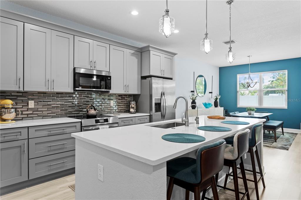 A modern kitchen features gray cabinets, a white quartz island, and a teal accent wall — 5220 94TH AVENUE N, PINELLAS PARK, FL