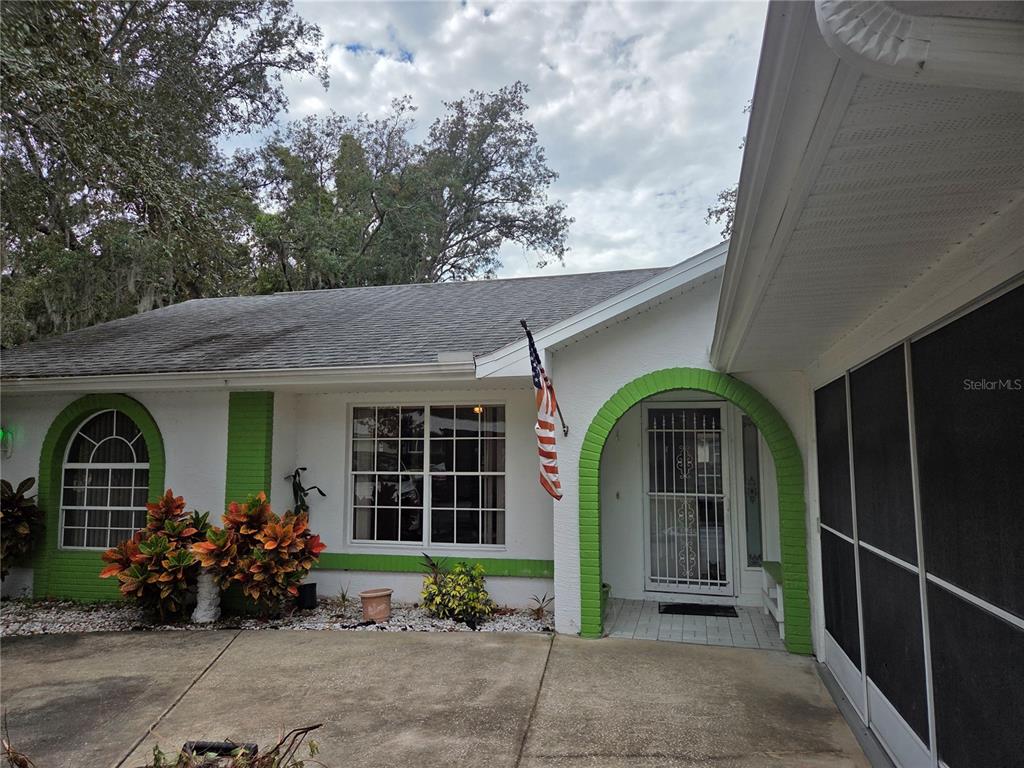 A white house exterior features green brick accents, an arched entryway, and a screened porch — 7605 LANDMARK DRIVE, SPRING HILL, FL