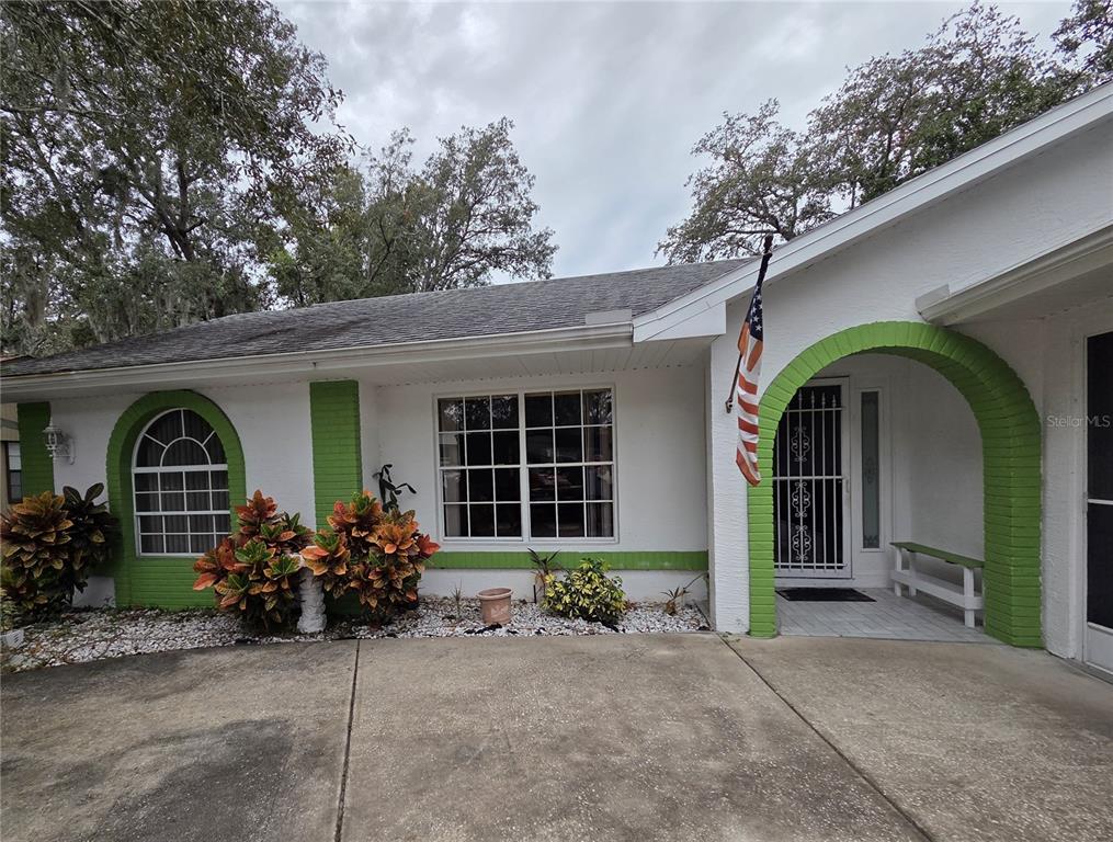 A white house exterior features green brick accents, an arched entryway, and a concrete driveway — 7605 LANDMARK DRIVE, SPRING HILL, FL