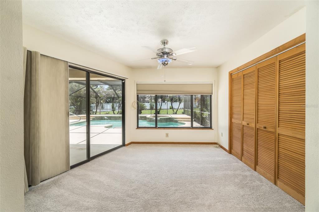 A carpeted room features a ceiling fan, sliding glass doors, and wooden louvered closet doors — 714 PENNYROYAL PLACE, BRANDON, FL