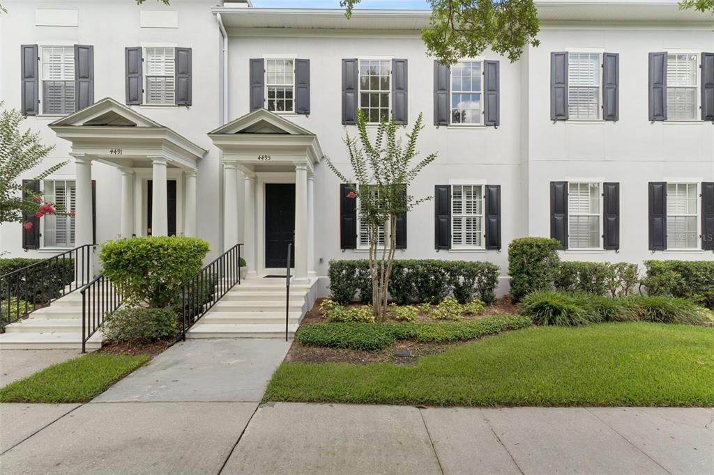 A white townhouse exterior features black shutters, columned entryways, and a manicured front lawn — 4495 TWINVIEW LANE, ORLANDO, FL