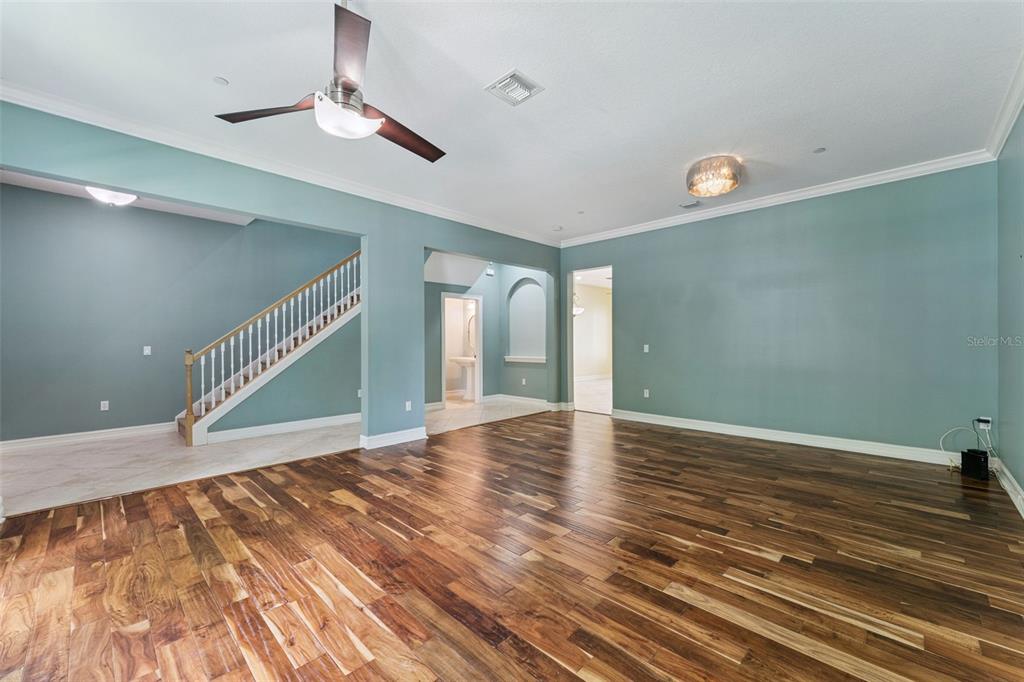 A spacious room features hardwood flooring, teal walls, a ceiling fan, and a staircase — 4495 TWINVIEW LANE, ORLANDO, FL