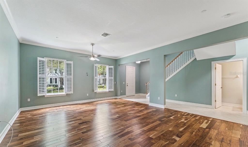 An empty room features hardwood floors, light blue walls, a ceiling fan, and a staircase — 4495 TWINVIEW LANE, ORLANDO, FL