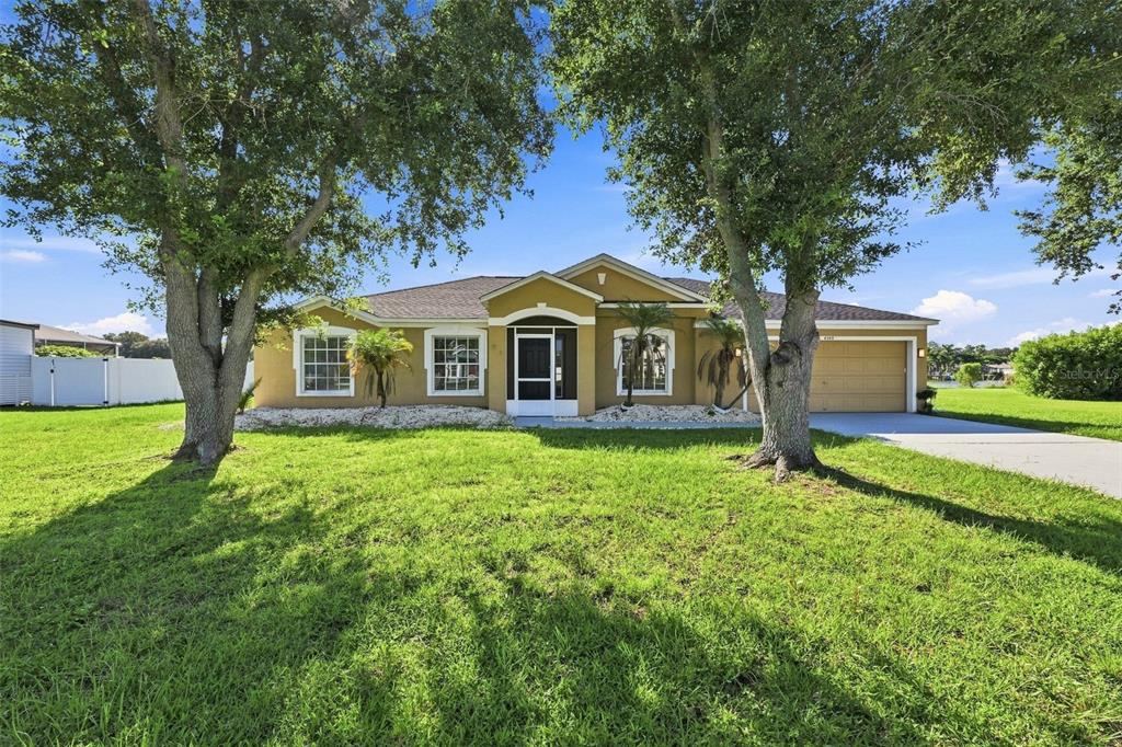 A single-story tan house with a two-car garage sits behind two large trees — 6505 CLAIR NEST COURT, APOLLO BEACH, FL