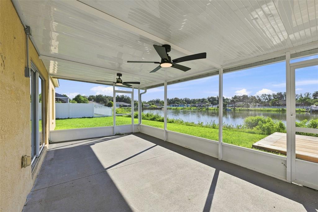 A screened-in concrete patio overlooks a lake with a wooden deck and grassy yard — 6505 CLAIR NEST COURT, APOLLO BEACH, FL