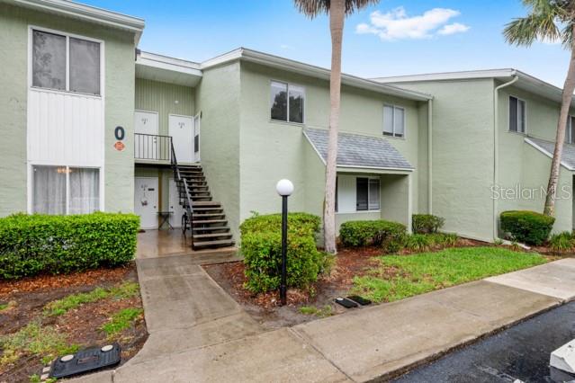 A two-story apartment building features light green stucco walls, a metal staircase, and landscaping — 631 SILVER PASS UNIT A, OCALA, FL