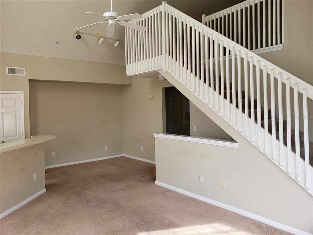 A living room with beige walls, brown carpeting, and a staircase with white railings — 9069 LEE VISTA BOULEVARD UNIT 1210, ORLANDO, FL