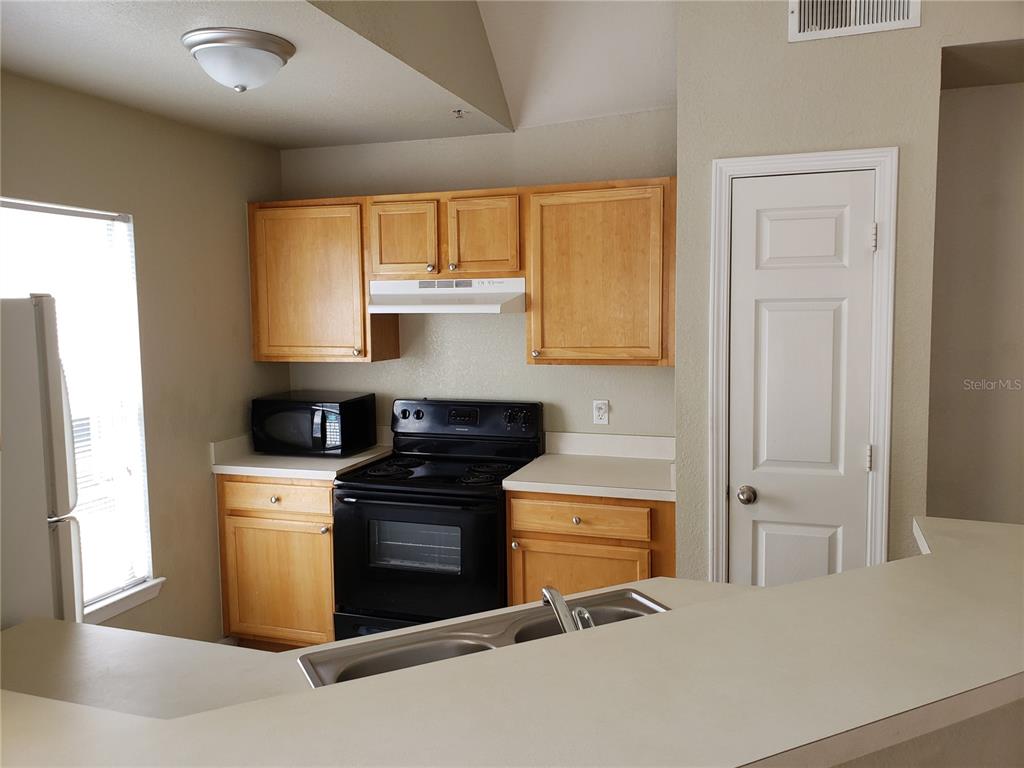 A kitchen features light wood cabinets, black appliances, and a white countertop with a sink — 9069 LEE VISTA BOULEVARD UNIT 1210, ORLANDO, FL