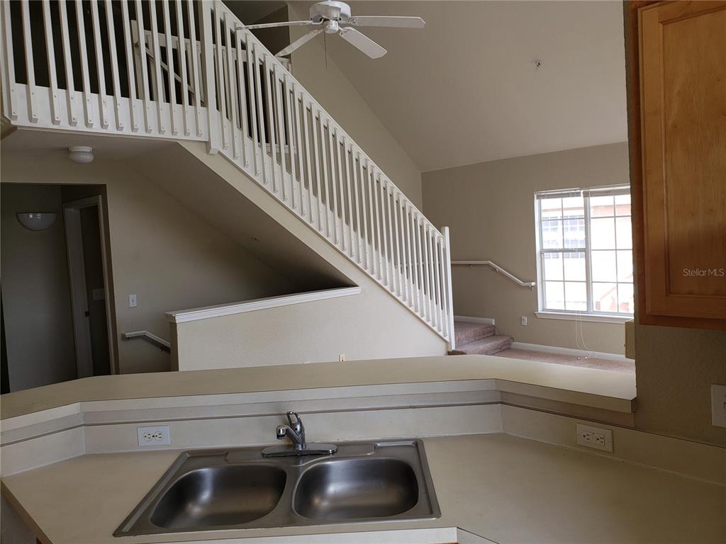 A kitchen sink and countertop overlook a living area with a staircase and ceiling fan — 9069 LEE VISTA BOULEVARD UNIT 1210, ORLANDO, FL
