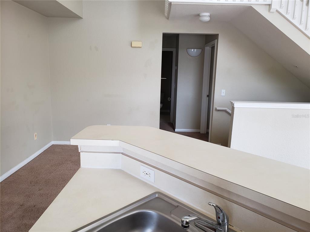 A kitchen sink and countertop overlook a carpeted living area with a staircase nearby — 9069 LEE VISTA BOULEVARD UNIT 1210, ORLANDO, FL