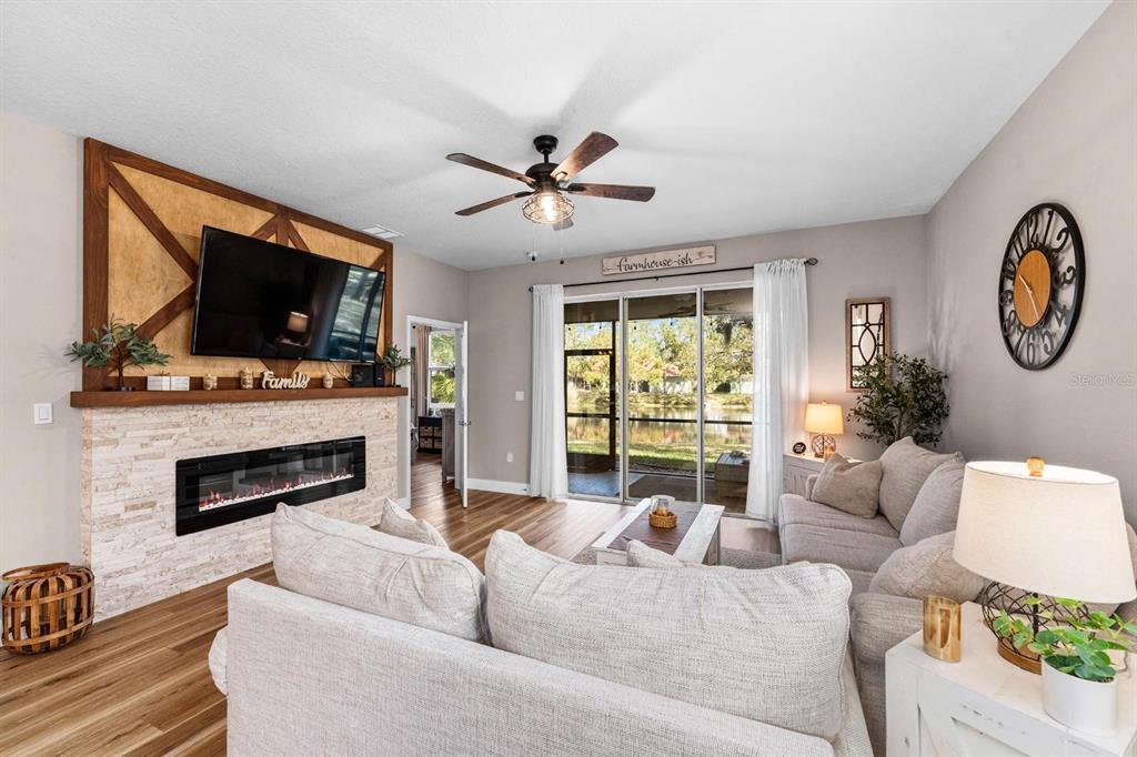 A living room features a stone fireplace, a wall-mounted television, and sliding glass patio doors — 128 51ST STREET CIRCLE E UNIT 7, PALMETTO, FL