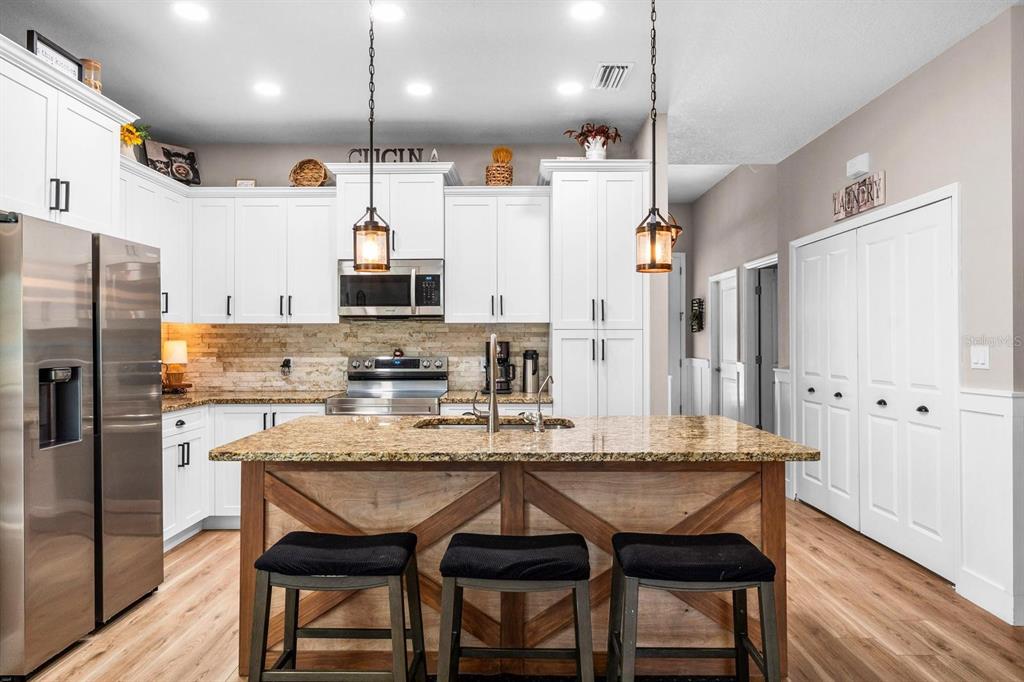 A kitchen features white cabinets, a granite-topped island with wood trim, and three bar stools — 128 51ST STREET CIRCLE E UNIT 7, PALMETTO, FL