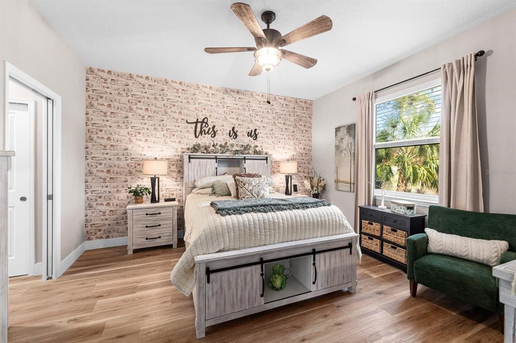 A bedroom features a faux brick accent wall, a wooden bed frame, and a ceiling fan — 128 51ST STREET CIRCLE E UNIT 7, PALMETTO, FL
