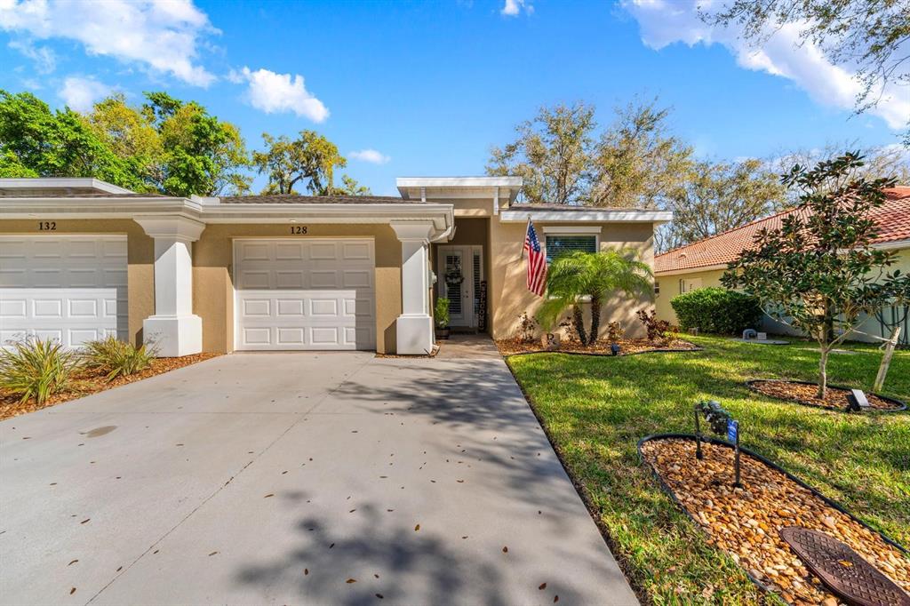 A tan single-story townhouse with a white garage door, a concrete driveway, and landscaping — 128 51ST STREET CIRCLE E UNIT 7, PALMETTO, FL
