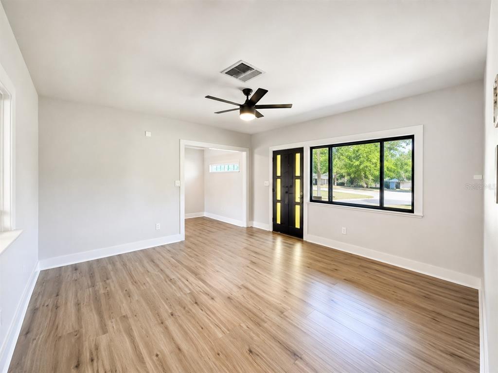 A living room with light-colored walls, wood-look flooring, a ceiling fan, and a black front door — 4200 BLUEFISH DRIVE SE, ST PETERSBURG, FL