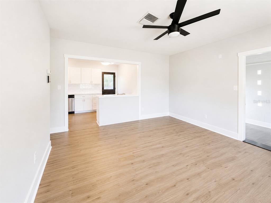 A living room with light wood flooring, a ceiling fan, and an open kitchen view — 4200 BLUEFISH DRIVE SE, ST PETERSBURG, FL