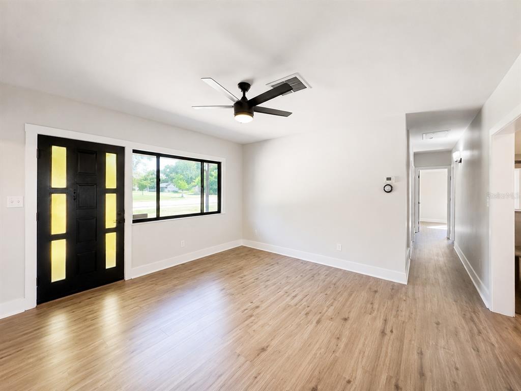 An empty room with light wood-look flooring, a black front door, and a ceiling fan — 4200 BLUEFISH DRIVE SE, ST PETERSBURG, FL