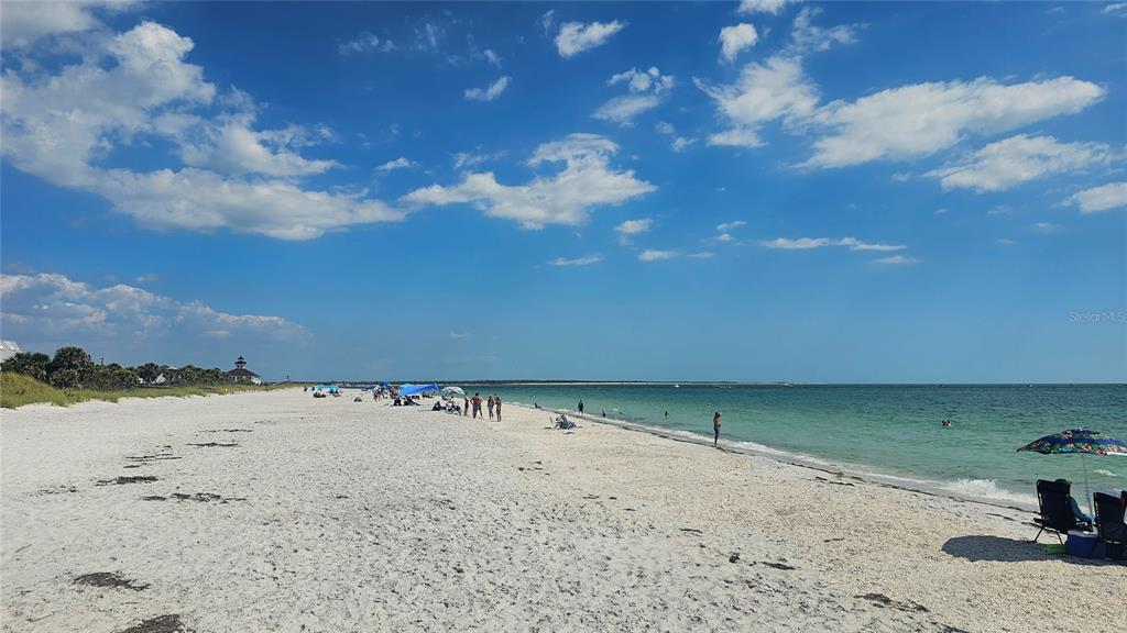 A wide, sandy beach with people, umbrellas, and a distant lighthouse under a blue sky — 5431 JOSLYN TERRACE, PORT CHARLOTTE, FL