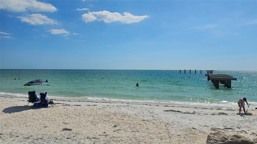 A sandy beach with a pier, a beach umbrella, and people enjoying the water — 5431 JOSLYN TERRACE, PORT CHARLOTTE, FL