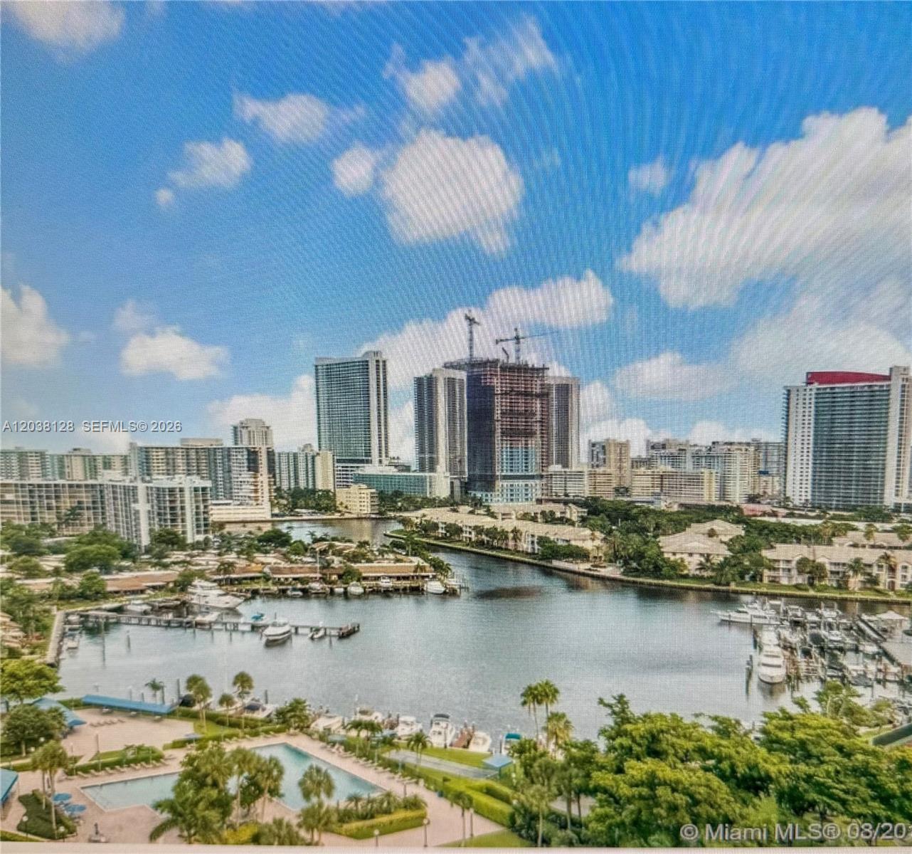 An elevated view of a marina, swimming pool, and surrounding high-rise buildings under a blue sky — HALLANDALE BEACH, FL