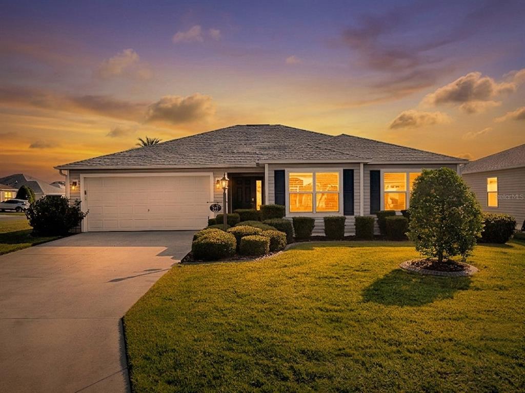 A single-story suburban house with a two-car garage and a landscaped front lawn at sunset — 843 CLIFFORD COURT, THE VILLAGES, FL