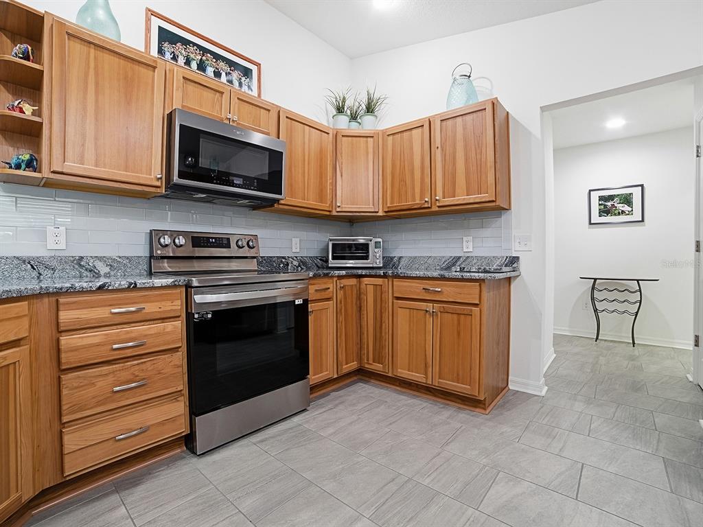 A kitchen features wood cabinets, stainless steel appliances, granite countertops, and gray tile flooring — 843 CLIFFORD COURT, THE VILLAGES, FL