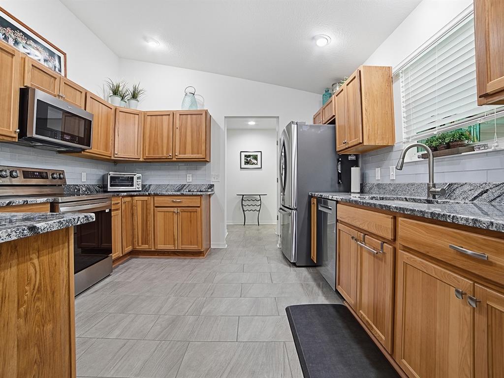 A kitchen features wood cabinets, granite countertops, stainless steel appliances, and gray tile flooring — 843 CLIFFORD COURT, THE VILLAGES, FL