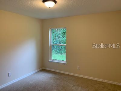 An empty bedroom with beige walls, tan carpeting, a single window, and a ceiling light — 1295 12TH STREET, ORANGE CITY, FL